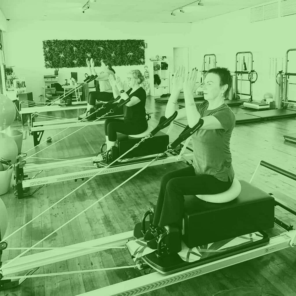 Women doing seated arm exercises in a Reformer Pilates class