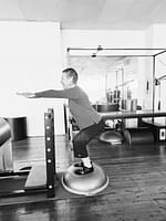smiling woman balancing on a bosu in a pilates class