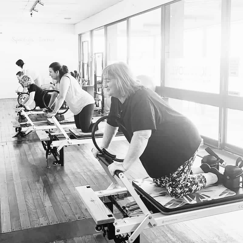 Women kneeling on reformers with a magic circle in a Reformer Pilates Class